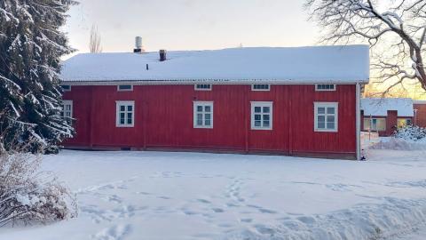 Talvisessa maisemassa puuverhoiltu punainen yksikerroksinen maatalo, Hatanpään pirtti, jonka yhdellä sivulla on viisi ikkunaa.