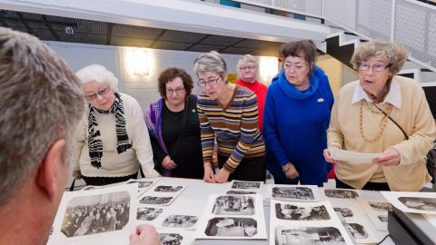 Seniorit katselevat pöydälle aseteltuja mustavalkoisia valokuvia.