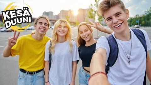 Neljä nuorta hymyilee kameralle auringon paisteessa. He ovat pukeutuneet kesäisiin värikkäisiin vaatteisiin.