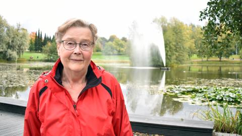 Henkilö seisoo puistossa. Takana on lampi ja suihkulähde.