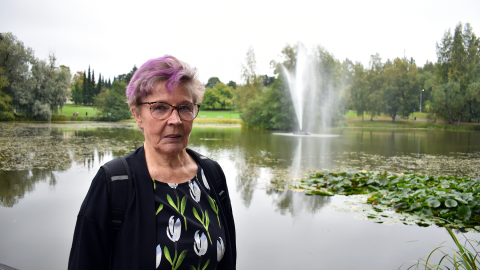 Sirkka-Liisa Jukarainen seisoo puistossa. Takana on lampi ja suihkulähde.