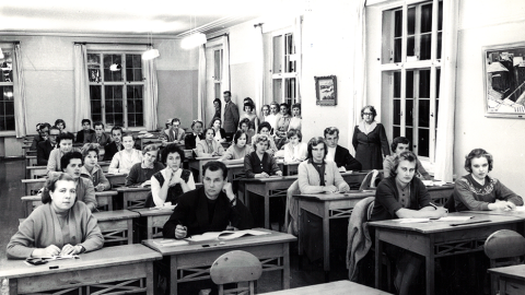 Henkilöt istuvat pulpeteissa luokkahuoneessa.