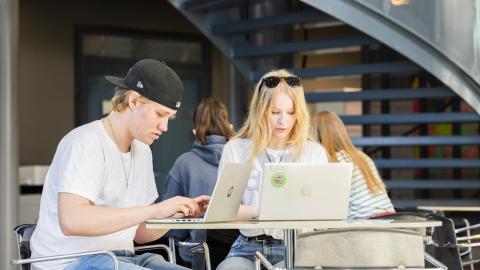 Kaksi opiskelijaa istuu pöydän ääressä ja työskentelee tietokoneilla. 