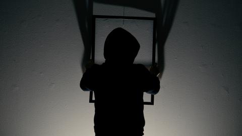 Tumma hahmo ripustaa tyhjää kehystä vaalealle seinälle.