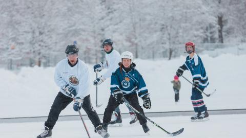 Neljä henkilöä pelaamassa jääkiekkoa luonnonjäällä.