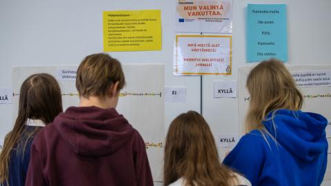 neljä nuorta seisoo seinän edessä, jossa lukee erilaisia vaikuttamiseen liittyviä lauseita