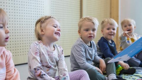 Happy children sitting on the floor in a row in a kindergarten.