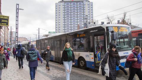 Useita ihmisiä kadulla kävelemässä ja taustalla bussi sekä korkea talo.