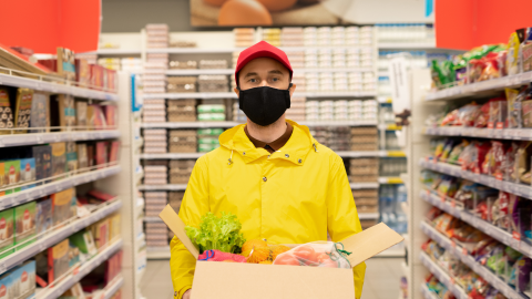 Nuori mies työskentelee ruokakaupassa ja kantaa pahvilaatikossa elintarvikkeita.