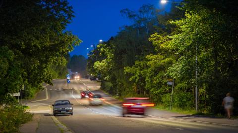 Valoja kadulla iltavalaistuksessa, vihreitä puita.