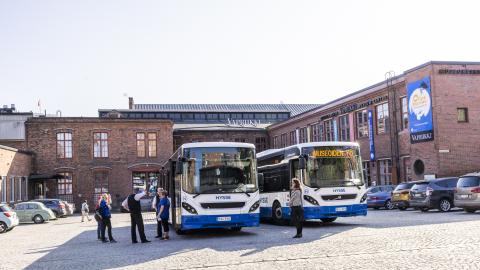 Kaksi sinivalkoista bussia rakennuksen pihalla. 
