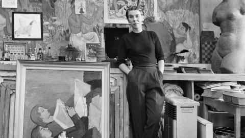 Mustavalkoinen valokuva, jossa nainen seisoo nojaten isoon maalaukseen. 