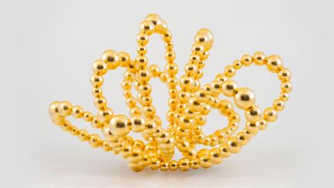  Kullatuista eri kokoisista helmistä koottu helminauha on taivuteltu avautuneen ruusun muotoon.