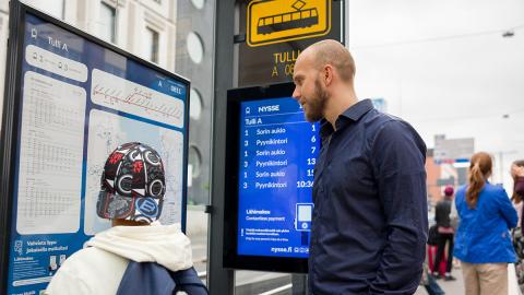 Mies ja poika tutkivat aikatauluja pysäkillä.