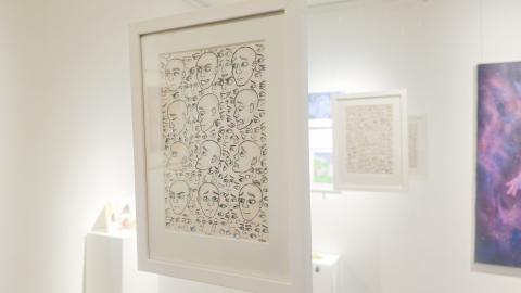 Yleiskuva galleriasta, jossa etualalla näkyy teos, jossa on piirrettynä erilaisia ilmeitä.