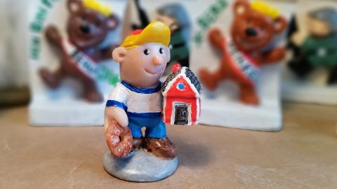 Pikkupoikaa esittävä pienoisveistos, jolla on punainen mökki kainalossaan.