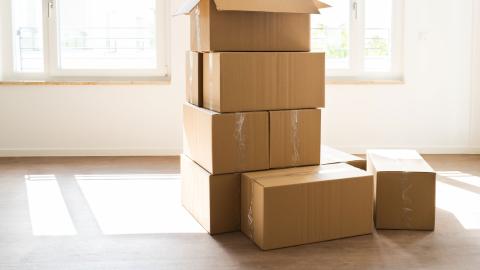 Useita pahvisia muuttolaatikoita päällekkäin tyhjässä huoneessa jossa kaksi ikkunaa ulos.