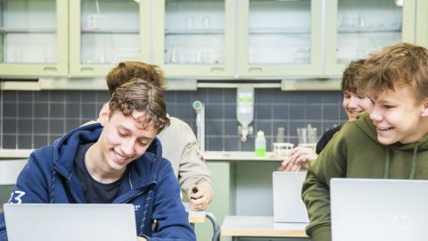 Neljä iloista nuorta miestä pulpettien äärellä.