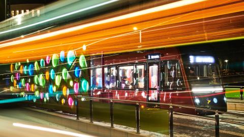 Kuvassa värikäs valotaideteos pysäkillä ja raitiotievaunu sen takana.