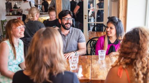 Five smiling people from Tampere are sitting at a table talking.
