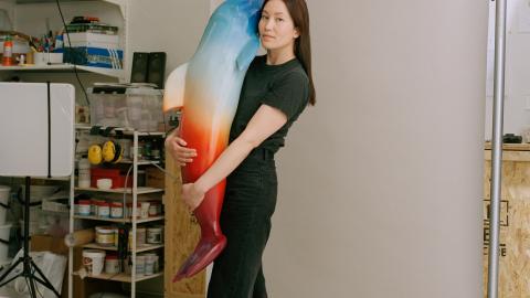 Tummahiuksinen nainen pitää sylissään delfiiniveistosta. 