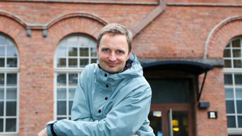 Mikko looks directly at the camera with the red brick Frenckell building in the background.
