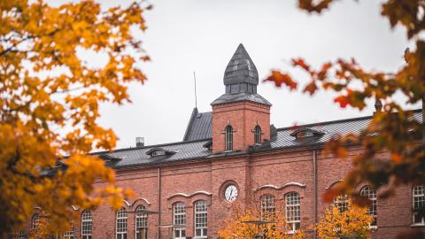 Punatiilinen rakennus ja sen kellotorni. Etualalla syksyisten puiden oksia.