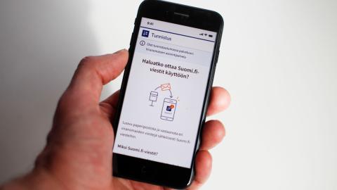 A person holding a mobile phone with instructions on how to activate Suomi.fi messages displayed on the screen.