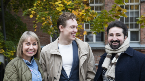 Kolme henkilöä seisoo syksyisen värikkään puun edessä.