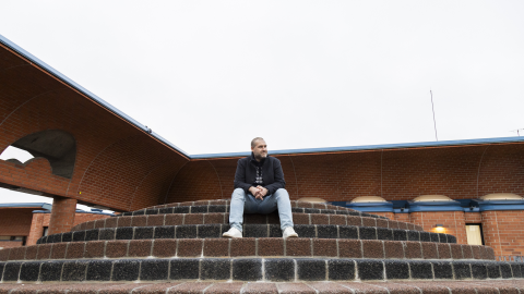 Henkilö istuu punatiilisen rakennuksen edessä portailla.