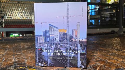 Kirjan kansikuvassa urbaani Tampereen keskusta. Kirja on kuvattu puulattialla, taustalla museon metallikaidetta.