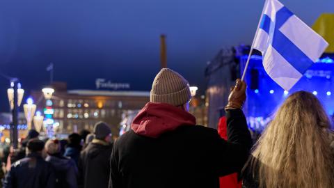 People in the evening at the winter time in the Central Square, with a person holding a Finnish flag. Finlayson building in the background.