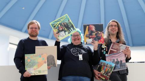 Kolme henkilöä seisoo iloisena vinylilevyjä käsissään.
