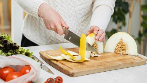 Ruonlaittaja leikkaa hunajamelonia. Pöydällä on myös tomaatteja ja salaattia.