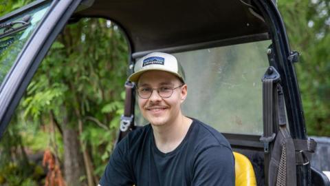 Henkilö istuu työkoneen kyydissä ja nojaa toisella kädellään rattiin.