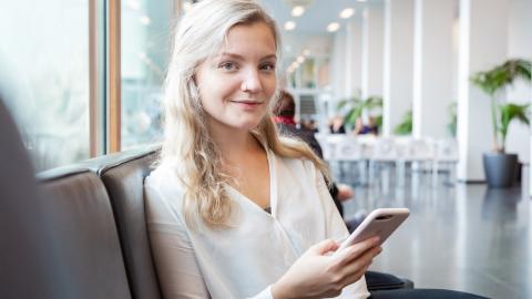 Nuori istuu oppilaitoksen käytävällä sohvalla ja pitelee puhelinta. Hän hymyilee.