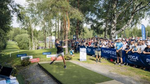 Pelaaja heittää frisbeegolf-kiekkoa yleisön katsellessa.