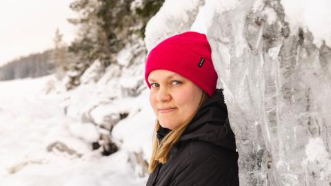 Punapipoinen henkilö nojaa jäiseen korkeaan kallioon.