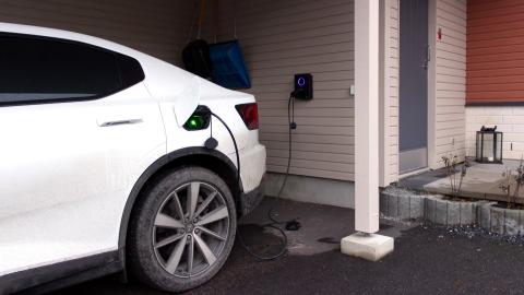 Valkoista sähköautoa ladataan autokatoksessa.