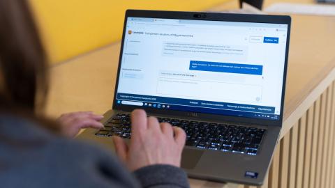 A person is studying the Entrepreneurship Advisory website on a laptop. The person is photographed from behind, with only a bit of hair, the right shoulder, and the hand visible. On the laptop screen, the webpage of the new service is displayed.