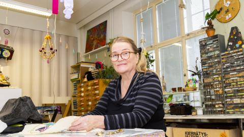 Raitapaitainen nainen tekee käsityötä Monitoimitalon kädentaitopajassa.