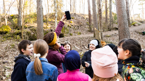 Aikuinen pitää kädellään desibelimittaria korkealla ilmassa ja lapset seuraavat tilannetta ympärillä.
