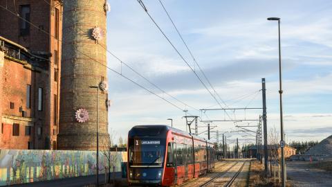 Kuvassa keskellä ratikka, vasemmalla piippu jossa kukiksta muodostuva teos.