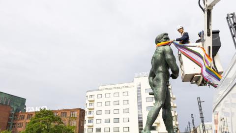 Pormestari Ilmari Nurminen seisoo nosturin lavalla turvakypärä päässään. Hän kietoo pride-väristä huivia Hämeensillan patsaan kaulaan.
