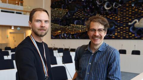 Mikael and Henrik pictured in the council chamber. In the background, a dark blue Pansy Sea artwork in dark blue and gold.