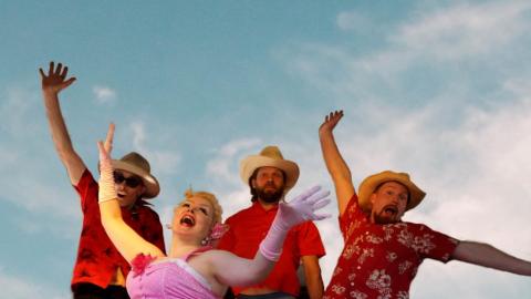 Happy band members with their hands raised in the air and a beautiful sky in the background.