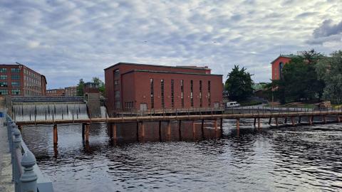 The photo shows a lightweight bridge below the red-brick power plant at Tammerkoski Rapids.