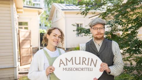 Kaksi vanhanaikaisiin asuihin pukeutunutta henkilöä pitelee käsissään Amurin museokortteli -kylttiä.