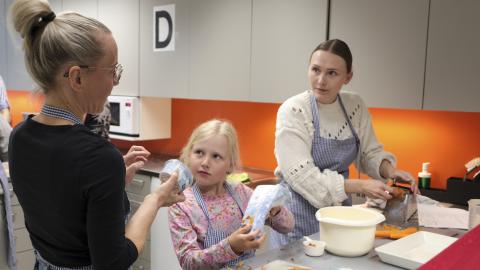 A teacher is helping a mother and daughter prepare a vegetarian meal at the Family Kitchen.