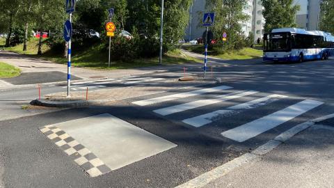 Suojatie ja hidasteet kuvattu kesällä ja bussi näkyy taustalla lähestyvän suojatietä.
